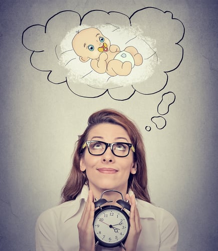 Portrait happy woman dreaming a baby looking up holding alarm clock isolated on gray wall background. Positive face expression emotion